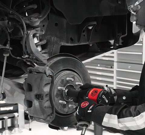 Worker using 1/2 Inch Air Impact Wrench Packin 960 Ft Lbs Of Raw Torque for wheel removal on a vehicle's brake assembly.