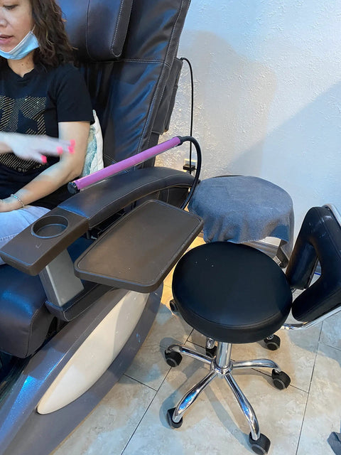 Woman receiving a manicure in a salon with reclining chair, footrest, and nail technician's stool.