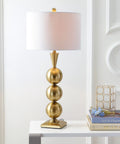 Brass Gold Stacked Orb LED Table Lamp 33 Inch Tall With White Linen Drum Shade on table next to books in living room