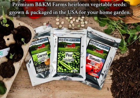 Close-up of B&KM Farms heirloom seed packets for carrot, pea, and tomato, placed on a wooden table with gardening tools and soil.