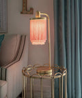 Framboise Fringe Shade Table Lamp With Gold Leaf Finish on a side table next to a sofa, adding elegance to a living room decor.