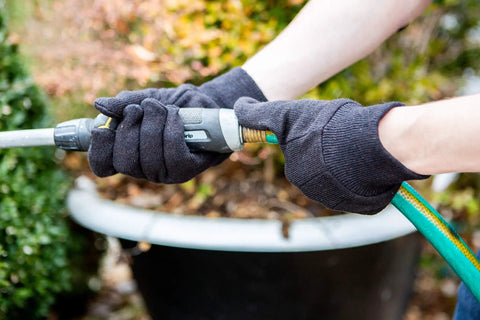 Person wearing Heavy Duty Cotton Work Gloves For Adults Unisex Regular Size Large Black Case Pack 300 Pairs using garden hose