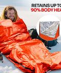 Person using Emergency Sleeping Bag 1 Pack For Survival Gear Waterproof Mylar Bivy Sack Emergency Blanket for outdoor warmth on snow.