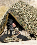 Multicam Camo Netting for Tactical Shelters and SmartFrame Systems in desert setup with soldier underneath aiming for concealment