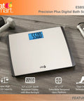 Digital Bathroom Scale 550 Pound Capacity With Extra Wide 15 Inch By 13 Inch Platform Stainless Steel Body Step On Technology Large Backlit LCD Readout Fingerprint Resistant Glass Base on wood floor with dumbbells.