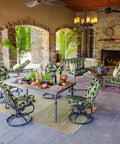 Outdoor patio dining set with cushioned swivel chairs, dining table set, and tropical plant-patterned cushions under a covered stone verandah.