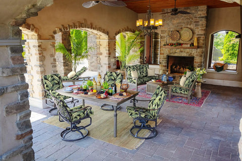 Outdoor patio dining set with cushioned swivel chairs, dining table set, and tropical plant-patterned cushions under a covered stone verandah.