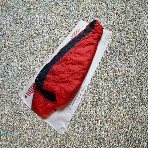 Lightweight Tyvek Tent Footprint Ground Cloth For Camping And Backpacking, breathable tarp under red sleeping bag on gravel.