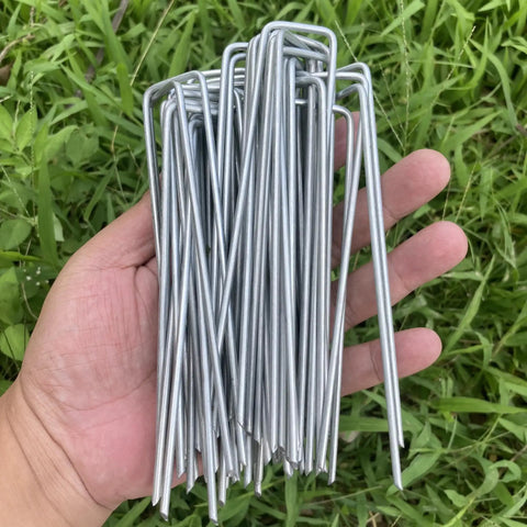 Hand holding sturdy 6 inch galvanized steel garden stakes for securing weed fabric landscape netting ground sheets fleece
