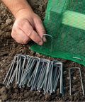 Hand installing 100 Pack 6 Inch Garden Stakes Galvanized Landscape Staples For Weed Barrier Fabric Heavy Duty Sod Pins