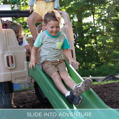 Child sliding down a green slide of Truck Climber Outdoor Playset For Kids, Backyard Playground With Slide And Climbing Wall.