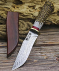 Damascus Steel Hunting Knife With Faux Antler Handle, 5.4 Inch Fixed Blade Skinner next to wooden sheath on wooden surface.