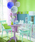 Colorful dining room with pastel chairs, round table, floral decor, and "SUMMER" wall decoration.