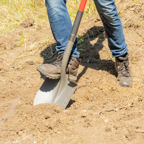 Person using Beefy 58 Inch Long Handle Round Point Garden Shovel With Steel Shaft Hardened Powder Coated Steel Head Textured Upper and Lower Grips Dual Riveted Blade Oversized Foot Pad In Red in a garden.