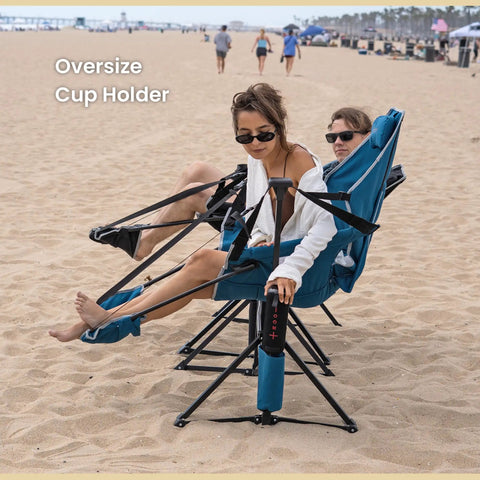 Two people sitting on a foldable hammock style camp chair with detachable footrest and padded headrest on sandy beach