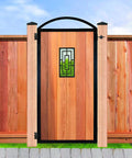 Wooden gate with wrought iron accents set in a cedar fence with decorative post caps, outdoors in a garden setting.