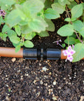 Raindrip S5600UB universal drip irrigation coupling on black plastic body attached to orange tubing in garden bed