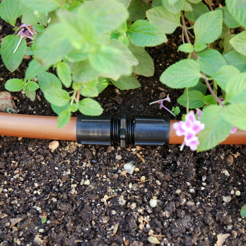 Raindrip S5600UB universal drip irrigation coupling on black plastic body attached to orange tubing in garden bed