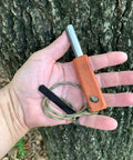Hand holding European Ferro Rod Fire Starter with Magnesium for Camping, 5-inch length, hardwood handle, paracord attached.