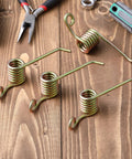 4 Pack Universal Power Rake Replacement Springs For Maxpower 330105 Dethatcher 16 Inch Mower Blade And Arnold 16 Inch Dethatching Replacement Blade With Easy Install Fits Most Lawn Mowers. Four metal coil springs on a wooden surface with tools.