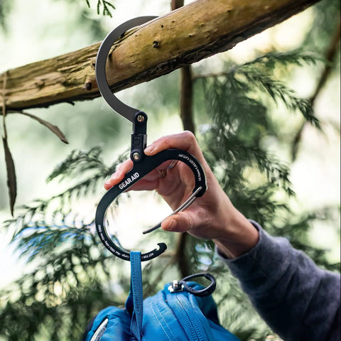 HeroClip Large Carabiner Clip And Hook For Camping, Backpacking, Garage Organization And Home Use, 3 In 1 Clip in Stealth Black hanging a blue backpack on a tree branch.