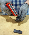 Master Magnetics red handheld magnet with ergonomic handle lifting a small black metal piece on a workbench
