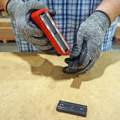 Master Magnetics red handheld magnet with ergonomic handle lifting a small black metal piece on a workbench