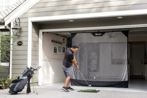Man practicing golf with 7 Foot Wide Baseball Softball And Golf Hanging Practice Net For Home Hitting Pitching And Driving Practice, Rolls Up Easily For Storage, Garage Door Mount, Durable Fiberglass Bottom Pole And Ball Catch in garage