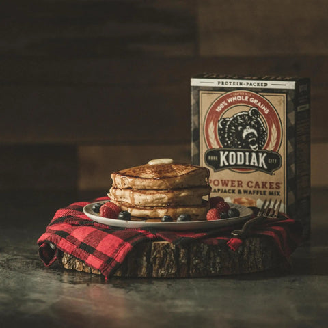 Stack of pancakes with butter and berries in front of Protein Pancake Power Cakes Buttermilk Mix Pack Of 6 Non GMO box.