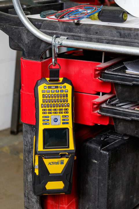 Built Tough Portable Handheld Label Maker With Rechargeable Battery hanging from a cart, showcasing its screen and keypad.