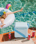 Powder Blue 11 Qt Tag-Along Two Strapped Picnic Style Cooler With Hands Free Crossbody Strap by poolside, cans nearby