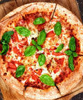 Top view of a freshly baked pizza topped with sliced tomatoes and basil leaves on a wooden board.