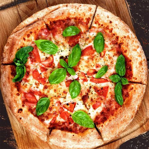 Top view of a freshly baked pizza topped with sliced tomatoes and basil leaves on a wooden board.