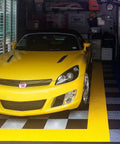Yellow car parked on Interlocking Garage Floor Tiles Diamond Pattern Non Slip Heavy Duty Copolymer 12X12 Inch Modular Tiles 48 Pack