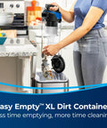 Woman using Easy Empty™ XL Dirt Container from Straight Up Powerful Upright Vacuum Cleaner for emptying debris into trash.