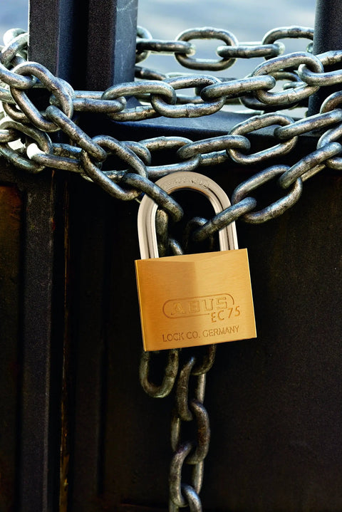 Solid Brass Padlock With Two Keys For Outdoor Use School Or Gym Lockers One And A Half Inch Wide Weather Resistant And Durable Keyed Different Built To Last For Gates Fences Lockers And Equipment secured to a chain gate.