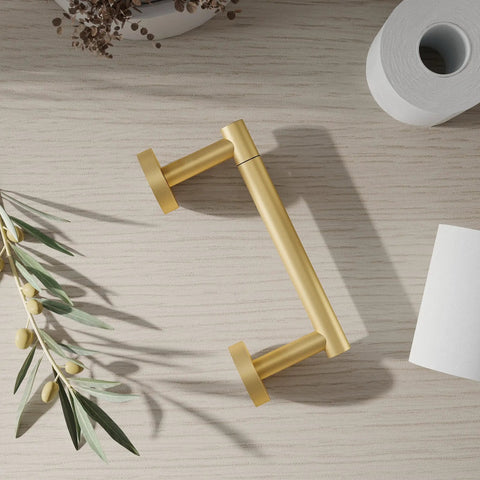 Gold 2 Pack Pivoting Toilet Paper Holder In SUS304 Stainless Steel Wall Mounted Double Post Tissue Roll Holder For Commercial Bathrooms And RVs Rustproof And Built To Last shown on a wooden surface with a roll of toilet paper nearby and decorative greenery.