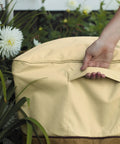 Veranda Water Resistant 26 Inch Square Patio Ottoman And Side Table Cover with padded handle being lifted outdoors