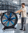 Person adjusting a 48 Inch Industrial Drum Fan With 17,660 CFM High Velocity Airflow, 750W Copper Motor on wheels in a factory.
