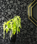 Black Flocked Skulls Wallpaper With Barbara Hulanicki Style behind green plant and decorative mirror, modern gothic decor.
