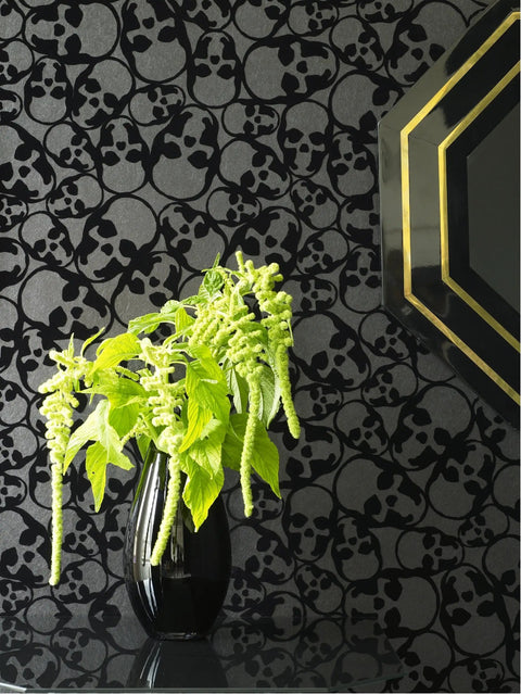 Black Flocked Skulls Wallpaper With Barbara Hulanicki Style behind green plant and decorative mirror, modern gothic decor.