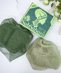 Authentic African Net Sponge 2 Pack Exfoliating Bath And Shower Loofah Sponge For Body And Face Go To Scrub For All Skin Types Travel Durable Polyester Olive Green And Light Green with packaging and flowers.