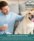 Man sitting on sofa holding phone next to a Labrador, MidWest Homes For Pets logo, family-owned text, cozy living room.