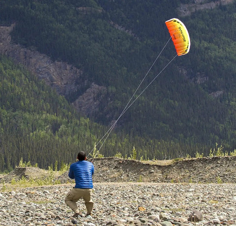 Person flying Synapse 140 Dual-Line Parafoil Kite in orange, enjoying smooth spins and dives amidst a mountain backdrop.