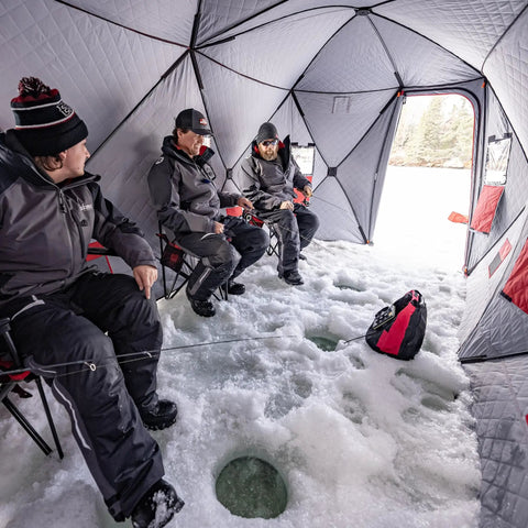 Three people using Quickfish Six Person Portable Pop Up Ice Fishing Shelter With Fully Quilted Insulation No Trip Door And Deluxe Anchors For Hell Of A Winter Setup In Red Black.