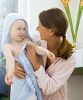 A mother holding her smiling child wrapped in a blue towel, enjoying warm water after a bath, highlighting comfort and care.