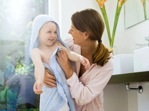 A mother holding her smiling child wrapped in a blue towel, enjoying warm water after a bath, highlighting comfort and care.