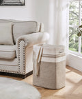 Beige storage basket by a sofa in a living room with a blanket draped over, showcasing All In One Cotton Rope Laundry Hamper And Storage Basket With Handles Collapsible Go To Organizer For Living Room Toys Blankets And Clothes Yellow Variegated 16 By 13 By 22 Inches.