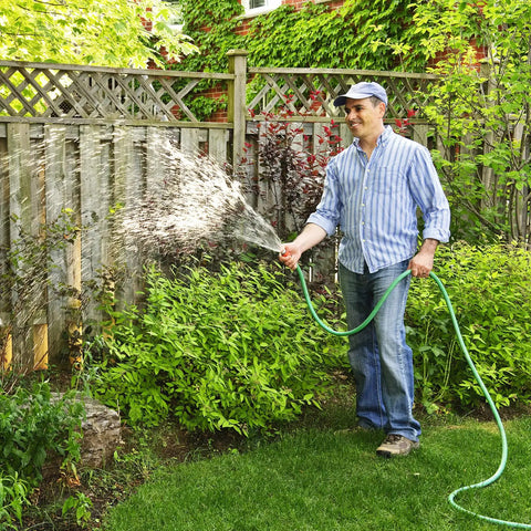 Person watering garden with green hose, showcasing irrigation use. Note: Clear Silicone Tubing visible in another context.