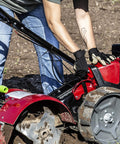Person using Pioneer Dual Direction Rear Tine Tiller With Counter Rotating And Standard Rotating Tines on soil, red black machine